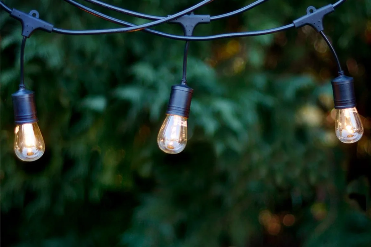 LSL string light lit outdoors against foliage at dusk